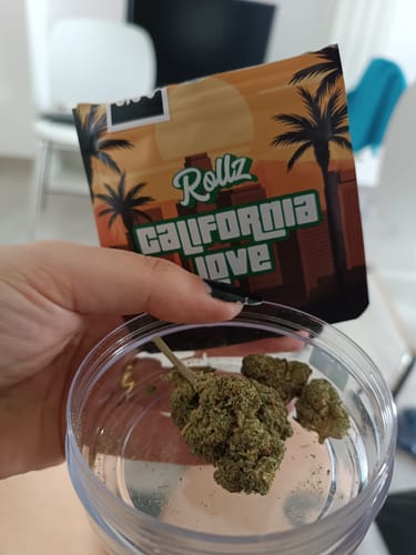 Customer displays California Love THCA Flower buds in a clear container next to the product packaging.