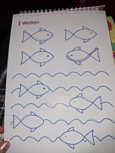 Kundenfoto eines Edubini Übungshefts, das eine Seite mit einer Nachzeichnungsübung für Fische und Wellen zeigt.