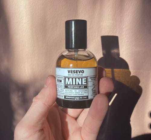 Recensore tiene in mano il flacone di profumo VESEVO con un liquido ambrato.