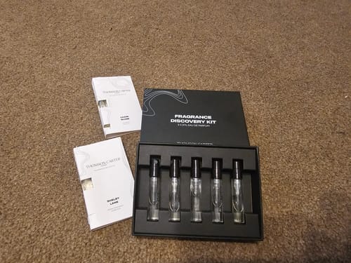 Customer's Fragrance Discovery Kit displayed on a carpet, with five sample vials in the open black box and two sleeves.