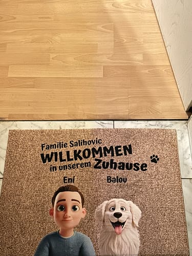 Rezensent zeigt die personalisierte 'Unser Zuhause'-Fußmatte mit einer Cartoon-Person und einem Hund vor der Haustür.