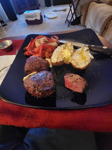 Customer's grilled USDA Choice Filet Medallions on a black plate, with one cut to show the pink center.