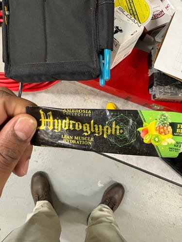 Customer's hand holding a single-serving packet of Ambrosia Hydroglyph Lean Muscle Hydration mix.