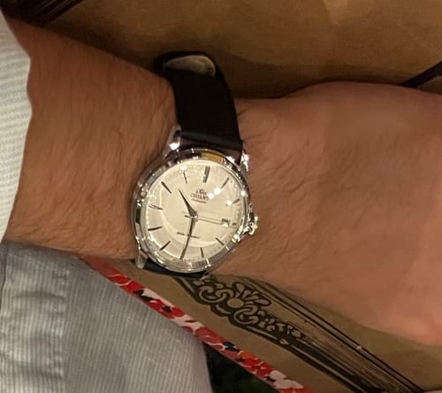 Primer plano del reloj Orient Bambino de un cliente en su muñeca, con caja plateada y correa de cuero.