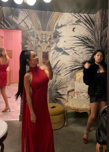 Customer taking a mirror selfie in the red Naked Halter Maxi Dress, showing its full length and long back ties.