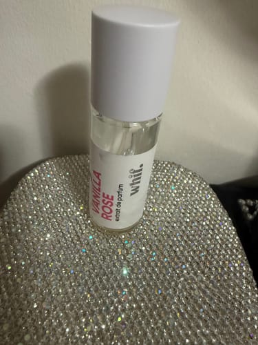 Reviewer's almost empty bottle of Vanilla Rose perfume sitting on a sparkly silver pouch.