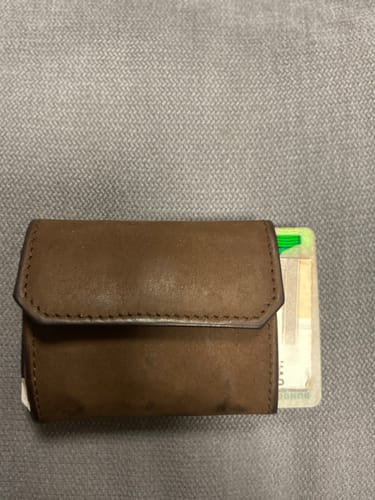 Customer's closed, brown Nano Boy Pocket card holder wallet lying on a grey surface with a card peeking out.