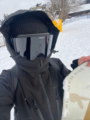 Reviewer wearing the black snow jacket with the hood up over their goggles on a snowy slope.
