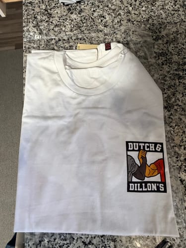Reviewer's new white 'Dutch and Dillon's' crewneck tee, folded on a countertop to show the handshake graphic.