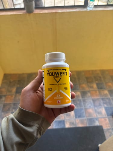 Customer holding a white bottle of YouWeFit Omega-3 Fish Oil with its yellow label visible.
