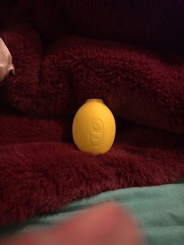 Customer's yellow Lem Clitoral Massager resting on a plush, dark red surface.