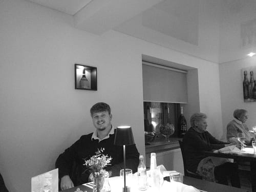 Ein vom Kunden mit der NUVINT Digitalkamera aufgenommenes Schwarz-Weiß-Foto einer Person an einem Restauranttisch.