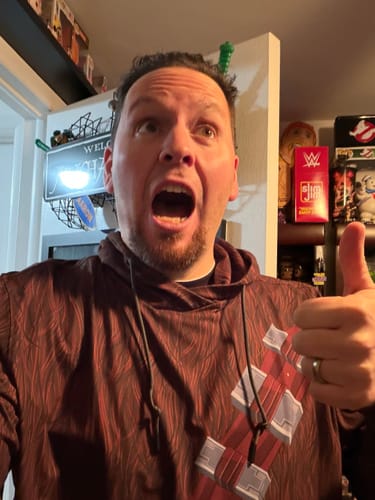 Reviewer wearing the brown, patterned 'The Chewie' Performance Hoodie makes a growling face and gives a thumbs-up.