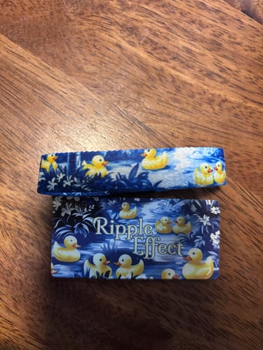 Customer's Ripple Effect bracelet and collector card on a wood surface, both showing a blue and yellow duck design.