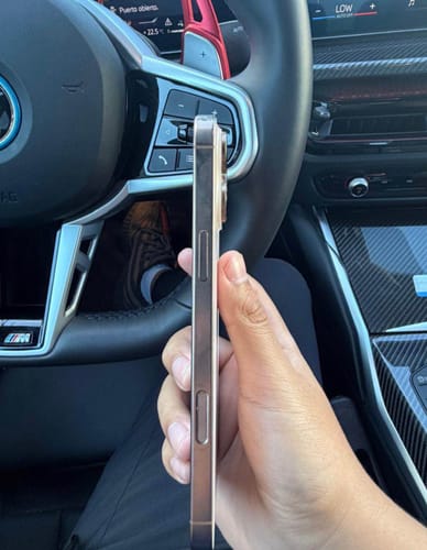 Cliente sosteniendo el costado de un IPHONE 16 PRO MAX color dorado dentro de un auto.