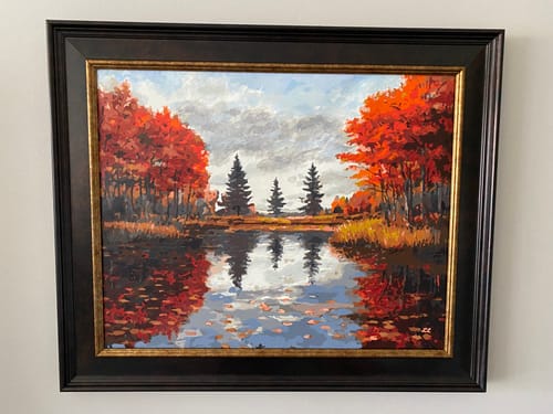Reviewer's completed Amber Reflections paint by numbers kit, framed and displayed on a wall, showing a vibrant autumn scene.