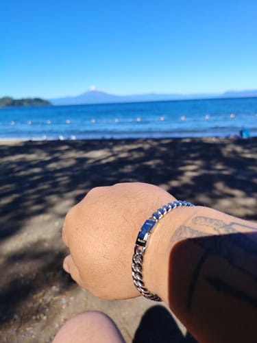 Cliente luciendo su Cadena Cuban Link de 8 mm en la muñeca, con una playa soleada de fondo.