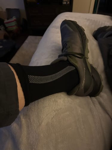 Customer wearing a black Men's Alpaca Sock, showing the fit and grey patterned band with an athletic shoe.