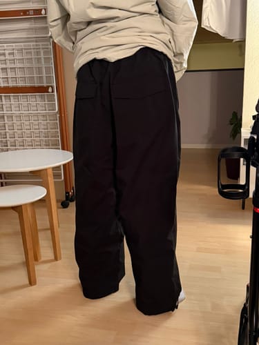 Reviewer from behind wearing the baggy black snow pants indoors.