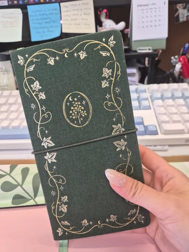 Reviewer holding the dark green Tsuki 'Secret Garden' Travel Notebook, showing the detailed gold foil botanical cover.