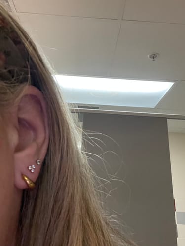 Close-up of a reviewer's ear wearing the gold Mini Drop Huggies in their first piercing.