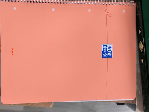Client avec son cahier à spirales OXFORD de couleur orange pastel, posé à plat.