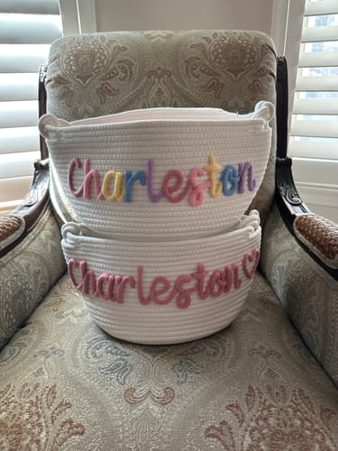 Reviewer's two personalized knitted baskets on a chair. One has "Charleston" in multicolor yarn; the other is in pink with a heart.