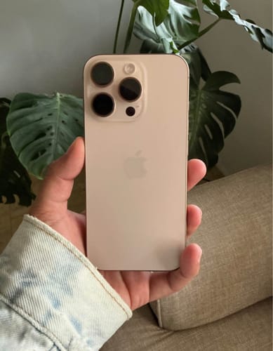Reseñador mostrando la parte trasera de un iPhone 16 Pro Max color claro que parece nuevo.