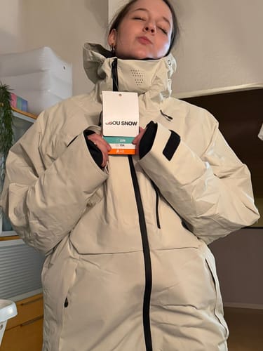 Reviewer wearing the oversized Khaki Snow Jacket indoors, showing the high collar and face vent while holding the tag.