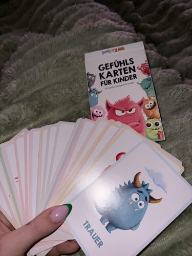 Ein Kunde hält die Edubini Gefühlskarten aufgefächert, wobei die Karte für 'Trauer' mit einem traurigen Monster zu sehen ist.