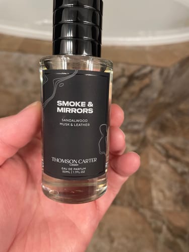 Reviewer's hand holding a clear bottle of Smoke & Mirrors Eau de Parfum, showing its black label.