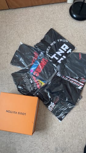 Customer's t-shirts from the TCG91 MYSTERY CASH BOX laid out on the floor, still in their clear packaging.