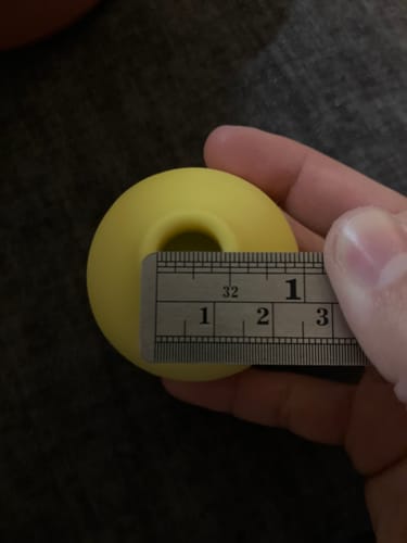 Reviewer measuring the opening of the yellow Lem Clitoral Massager, showing a width of 1/2 inch on a ruler.