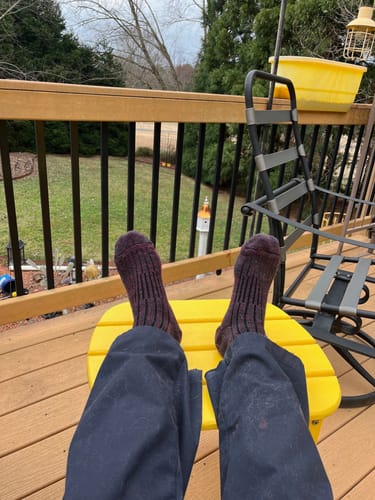 Customer relaxing on a deck with feet up, wearing thick, warm violet Joey Crew Socks.