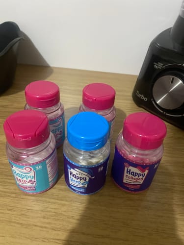 Um pote de Melatonina Happy Sleep com tampa azul entre outros frascos de suplemento sobre uma superfície de madeira.