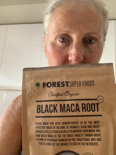 Reviewer holds up a brown paper bag of Certified Organic Black Maca Powder.