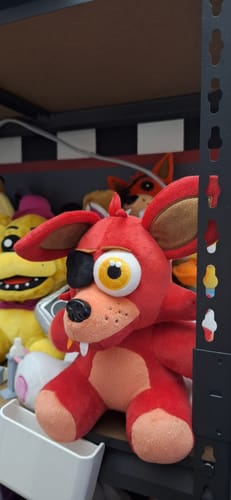 Customer's red Foxy plush from Five Nights at Freddy's sitting upright on a shelf with other toys.