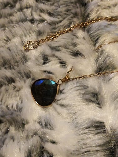 Pendentif en labradorite d'une cliente sur sa propre chaîne dorée, posé sur une surface en fourrure blanche.