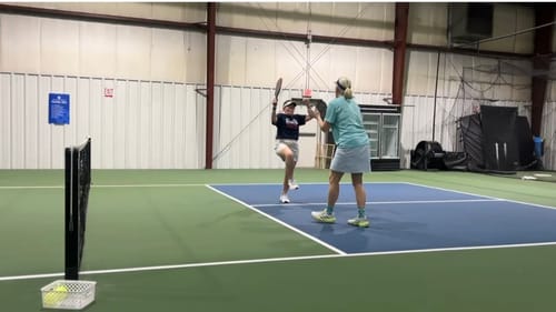 Reviewer in mid-air hitting a shot on an indoor pickleball court while wearing white MUUV Flow pickleball shoes.