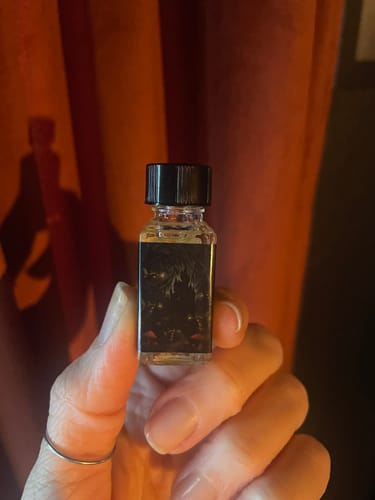 Close-up of a reviewer holding the Dark Realms scent, a small bottle with a dark label.