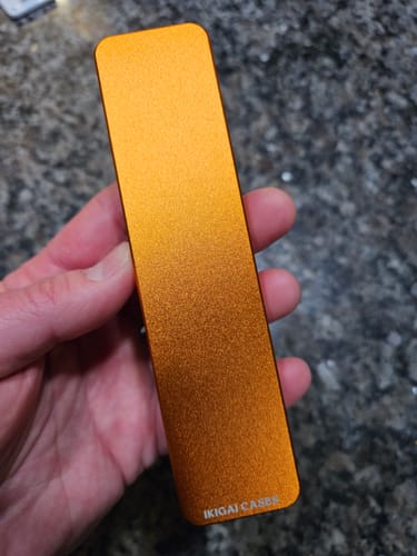 Reviewer holding the closed, orange metallic Weekly Case in their hand over a dark counter.