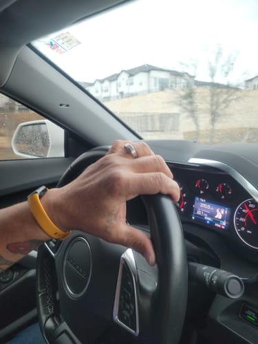 Customer's hand on a steering wheel, wearing the silver-colored Beveled Edge Band on their ring finger.