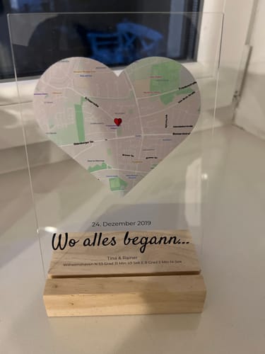 Rezensent zeigt die personalisierte Acryltafel mit herzförmiger Karte, die auf einem Holzsockel steht.