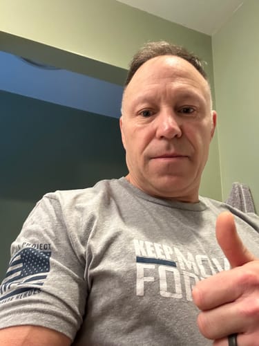 Reviewer gives a thumbs-up while wearing the grey 'Keep Moving Forward' t-shirt, showing the design and sleeve patch.