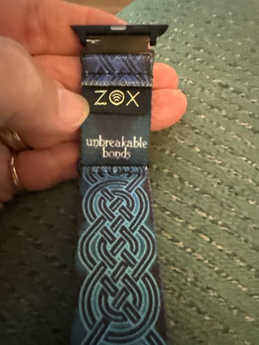 A close-up of a reviewer's hand holding the blue, patterned watchband connected to the black adapter.