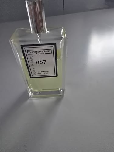 Customer's clear bottle of 987 perfume with a silver cap, set on a plain grey surface.