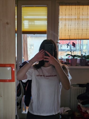 Reviewer in a mirror selfie wearing the white 'reading is sexy' graphic baby tee.