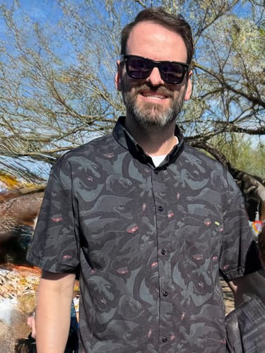 Reviewer smiling outdoors while wearing the dark 'Unleash the Fury' short sleeve shirt with a Toothless pattern.