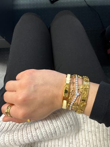 Rezensent trägt den beigen Agapi Armreif am Handgelenk, gestapelt mit anderen goldenen Armbändern.