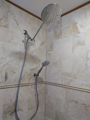 Customer's chrome handheld shower head installed in a tiled shower, part of a dual setup with a rain shower head.